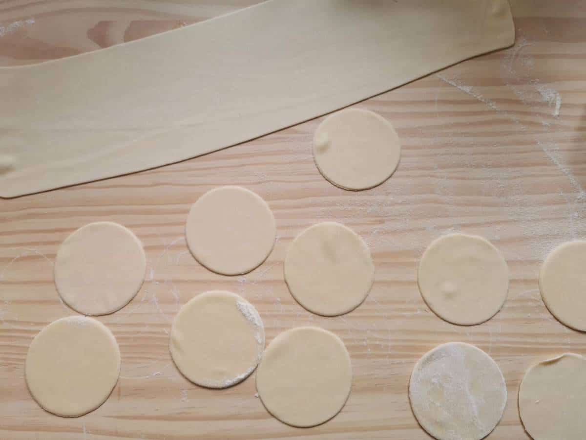 A sheet of pasta dough and some dough circles on a wood work surface.