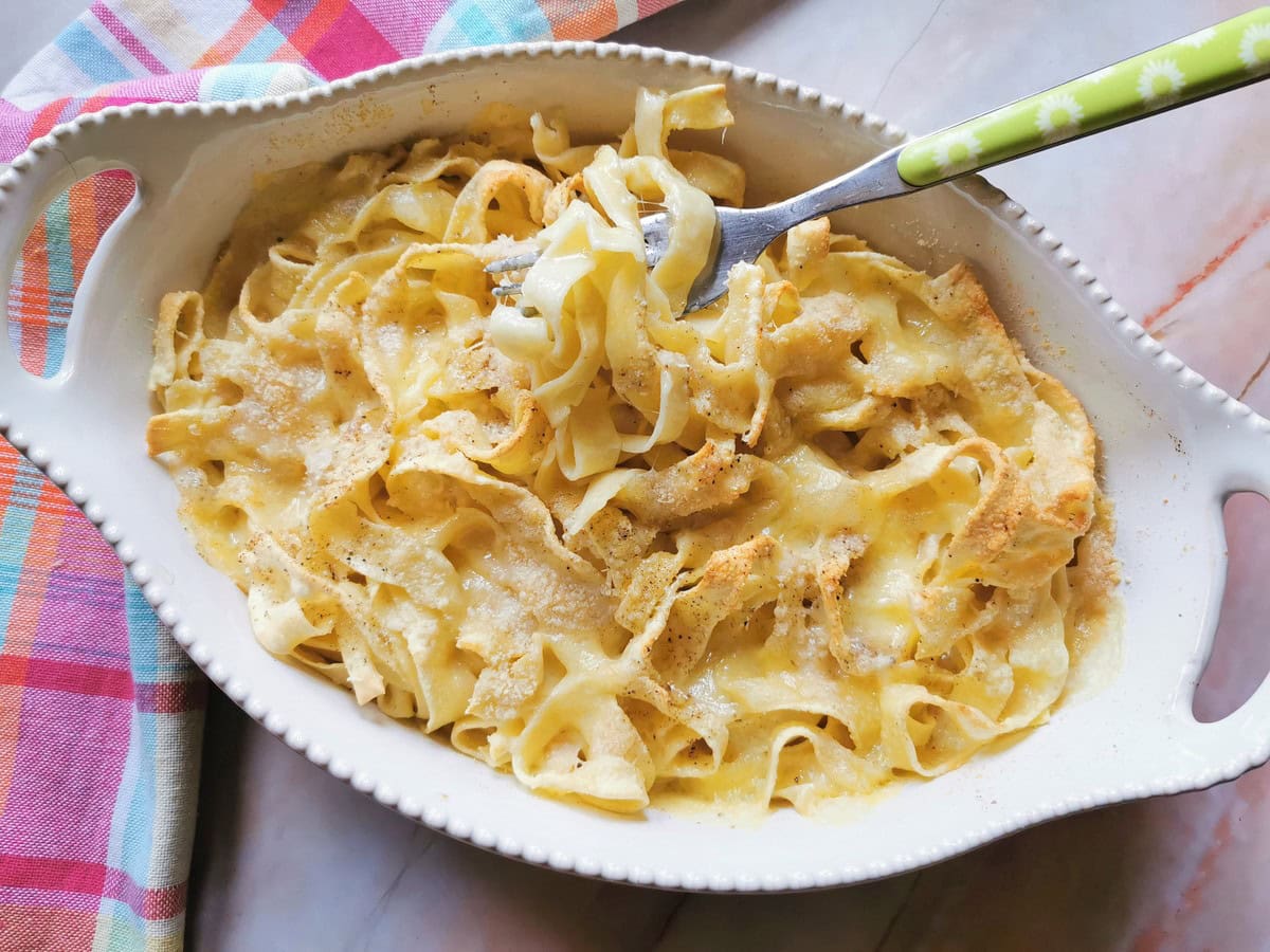 Ready oven baked tagliatelle with Fontina cheese in white oval oven dish.