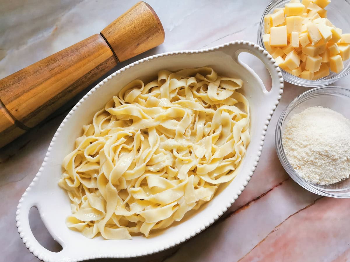 Cooked tagliatelle in white oval oven dish and Fontina cubes and grated Parmigiano in glass bowls.