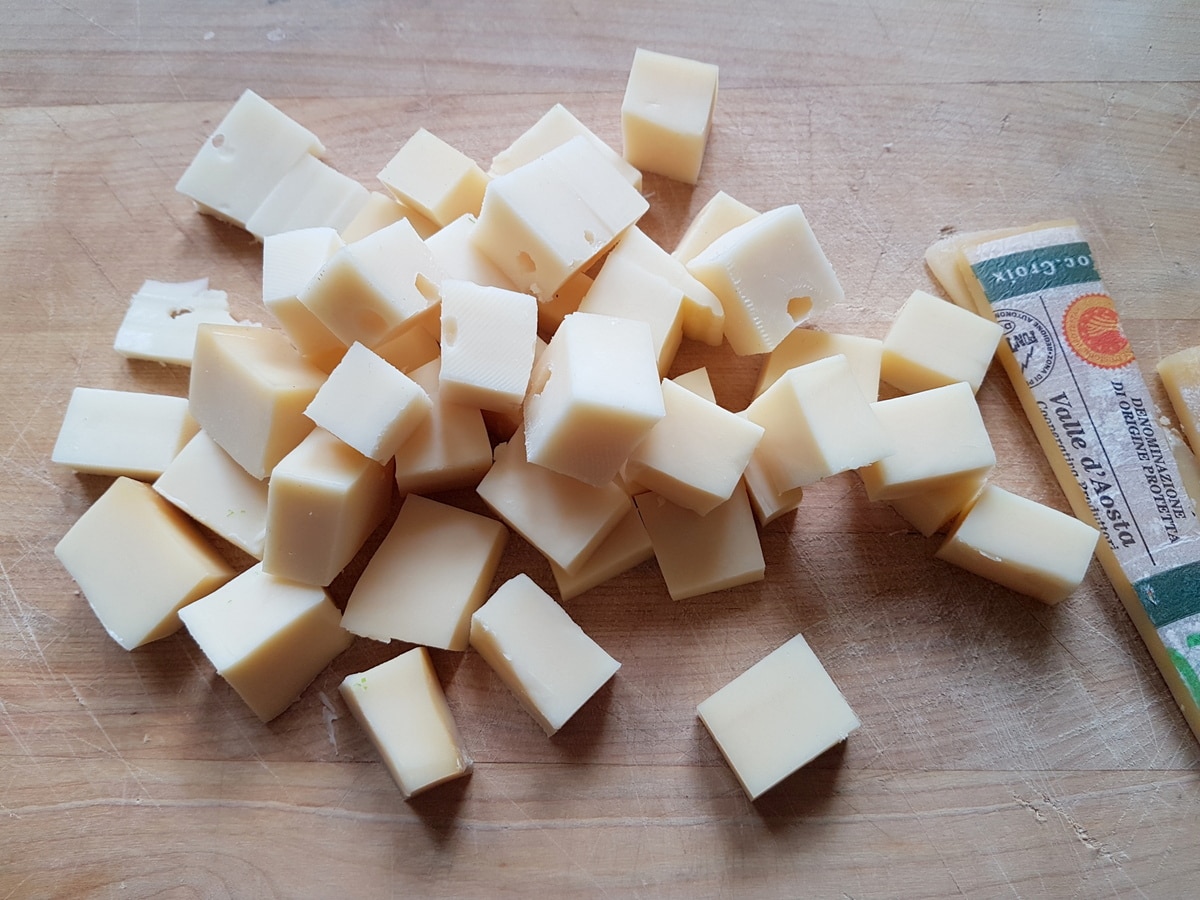 Fontina cheese cut in cubes on a wooden board.