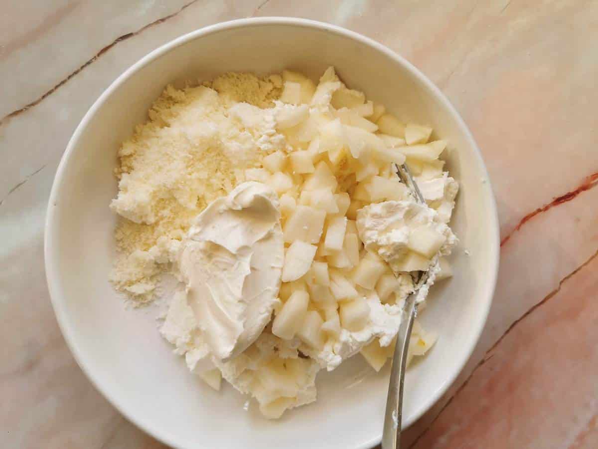 Mashed ricotta, mascarpone, grated parmigiano and pieces of fresh pear in white bowl.
