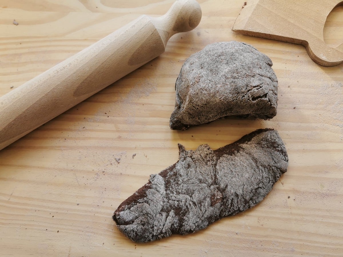 A flattened piece of chocolate ravioli dough next to a ball of dough and a rolling pin on a wood work surface.