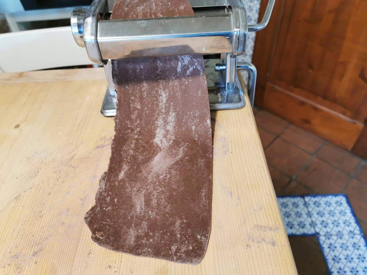 A sheet of chocolate pasta dough passing through a pasta machine.