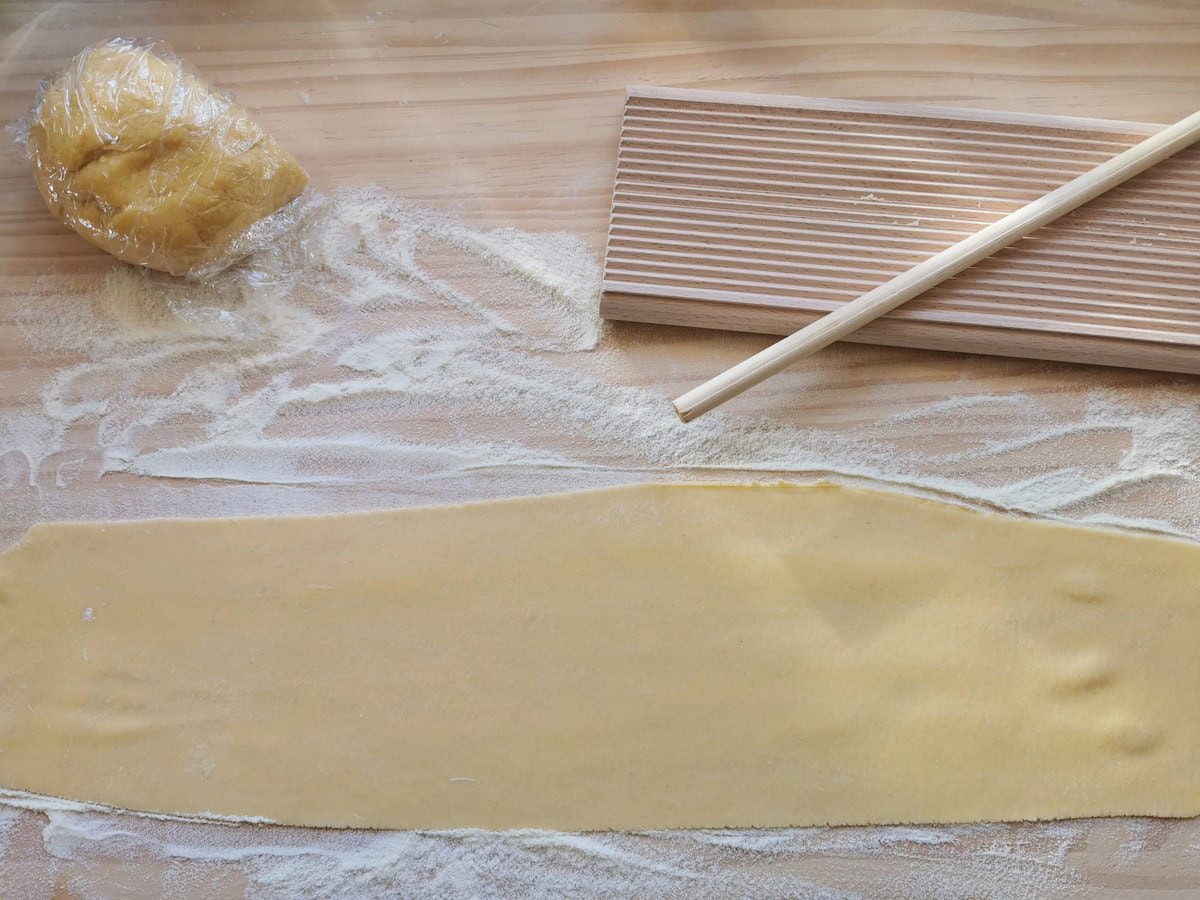 Sheet of pasta dough on flour dusted wood surface with gnocchi board.