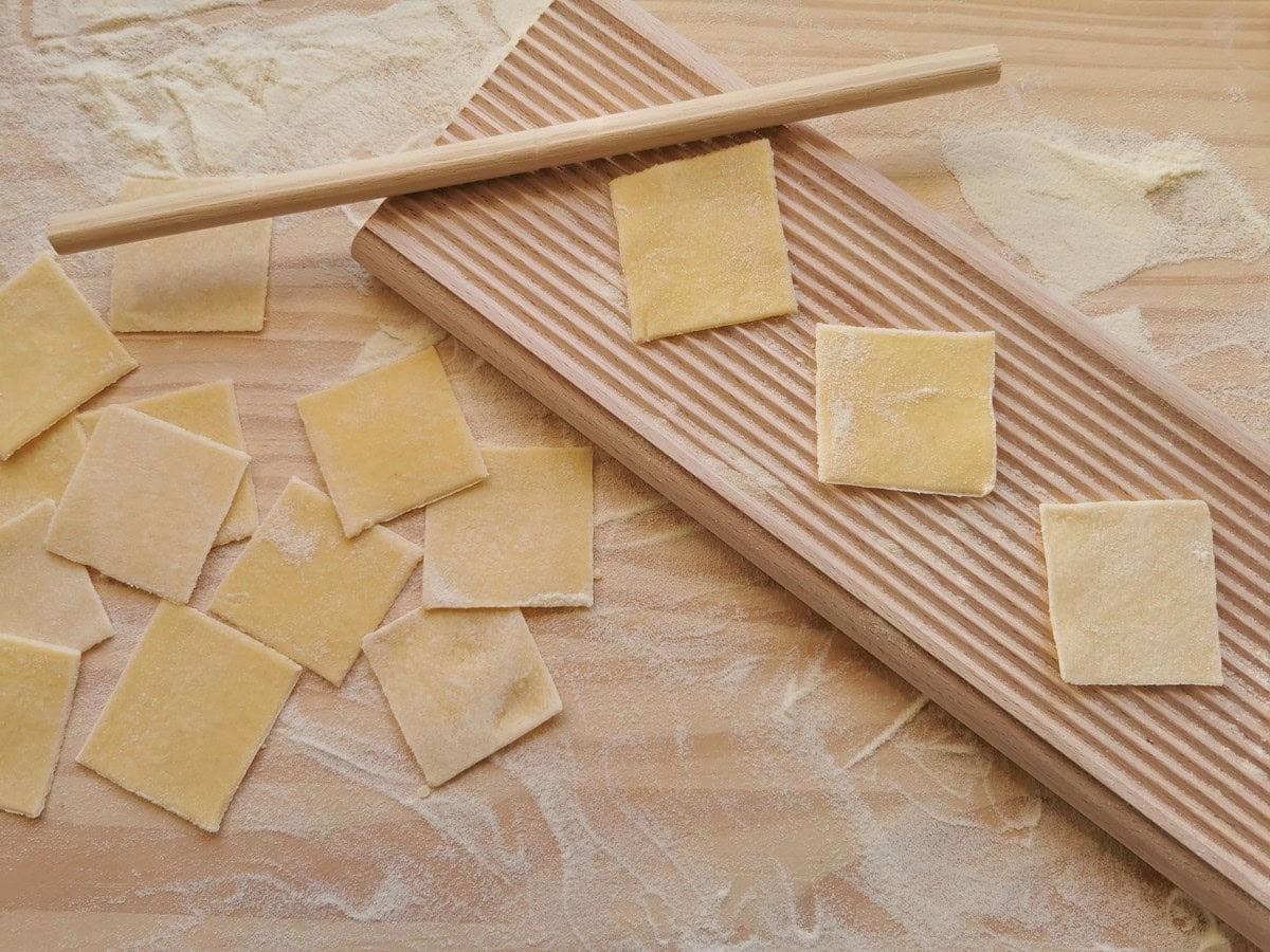 Squares of pasta dough on wood surface and gnocchi board.