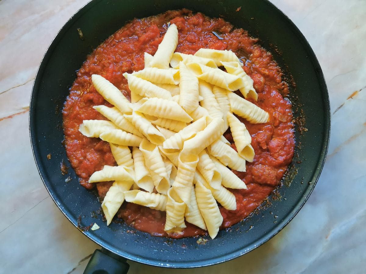 Cooked homemade garganelli pasta in skillet with sausage ragu.