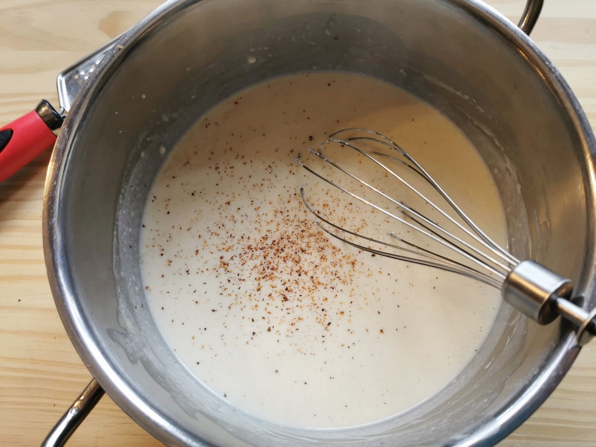 Whisking in nutmeg to the béchamel sauce.