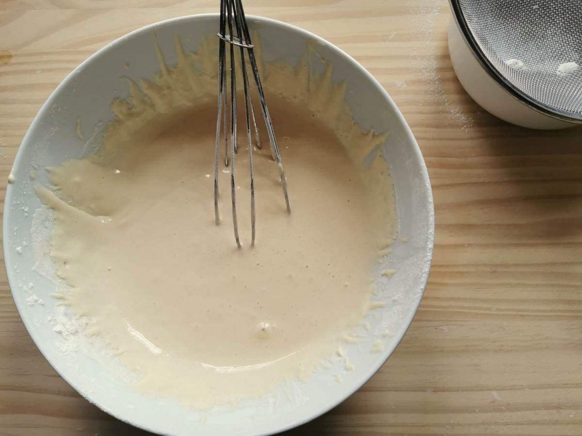 Batter for Italian teardrop dumplings (chnèfflènè) in white bowl with whisk.