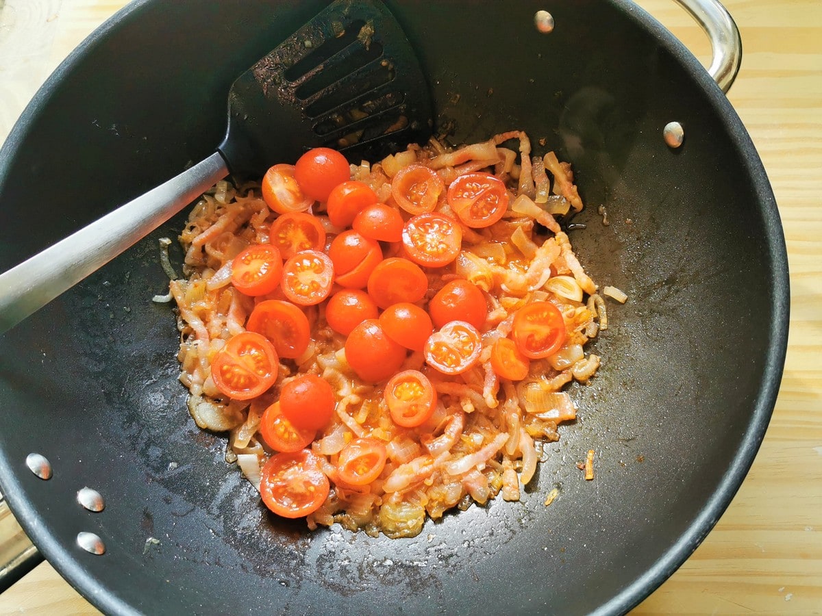 Halved cherry tomatoes in deep frying pan with shallots and guanciale.