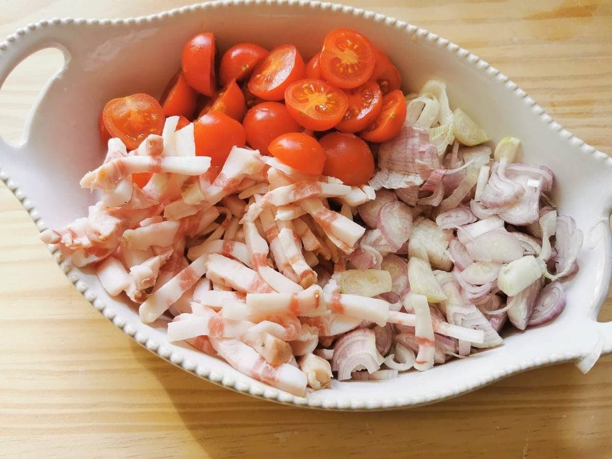 Prepared shallots, guanciale and cherry tomatoes in white bowl.