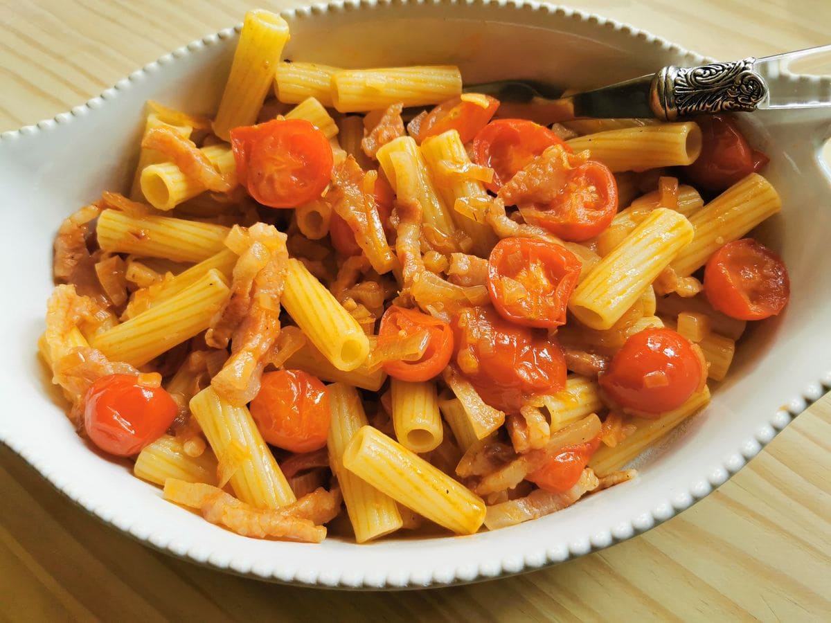 Rigatoni pasta with shallots and guanciale in white serving dish.