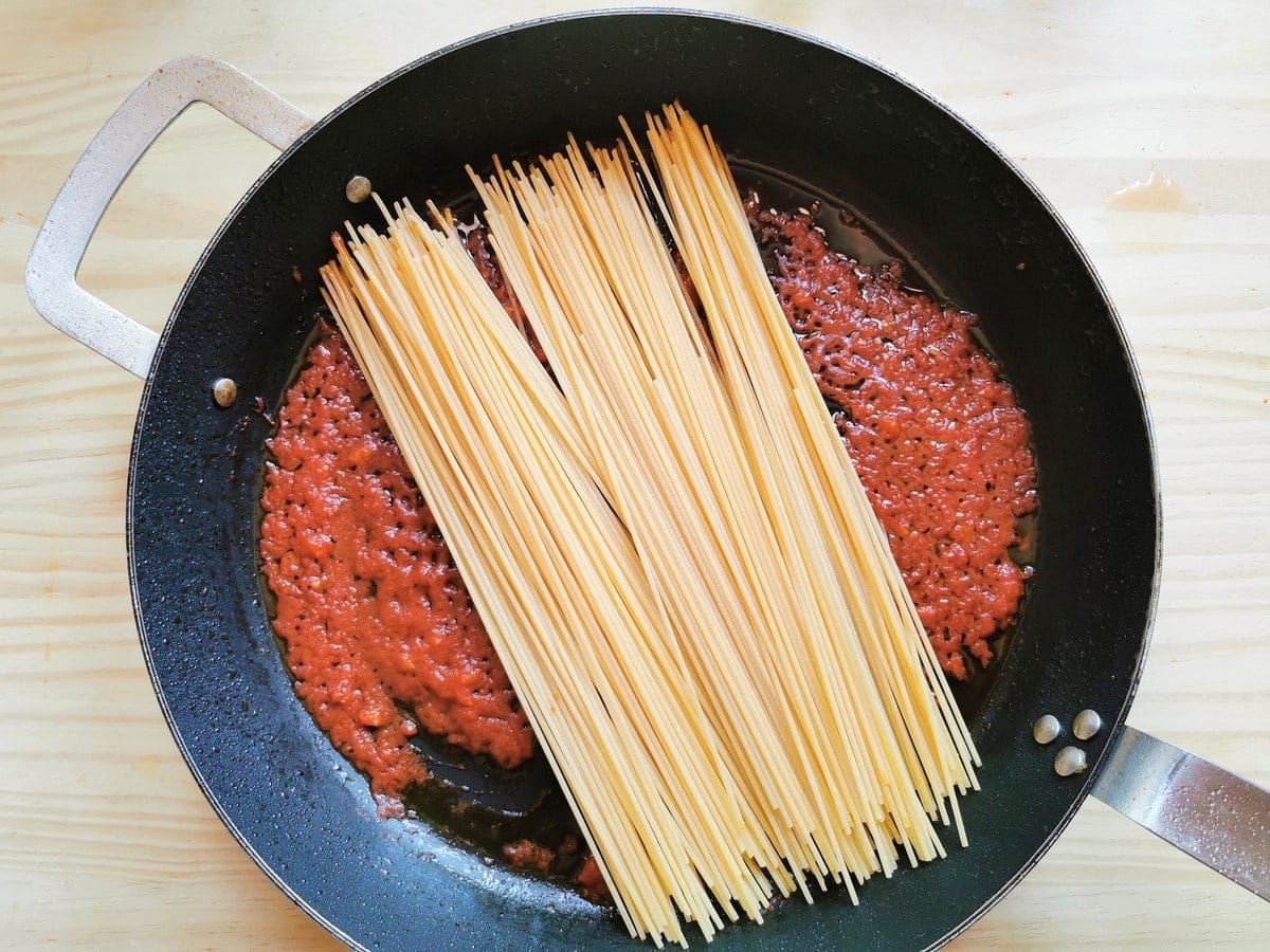 Uncooked spaghetti in cast iron skillet on top of cooked passata.