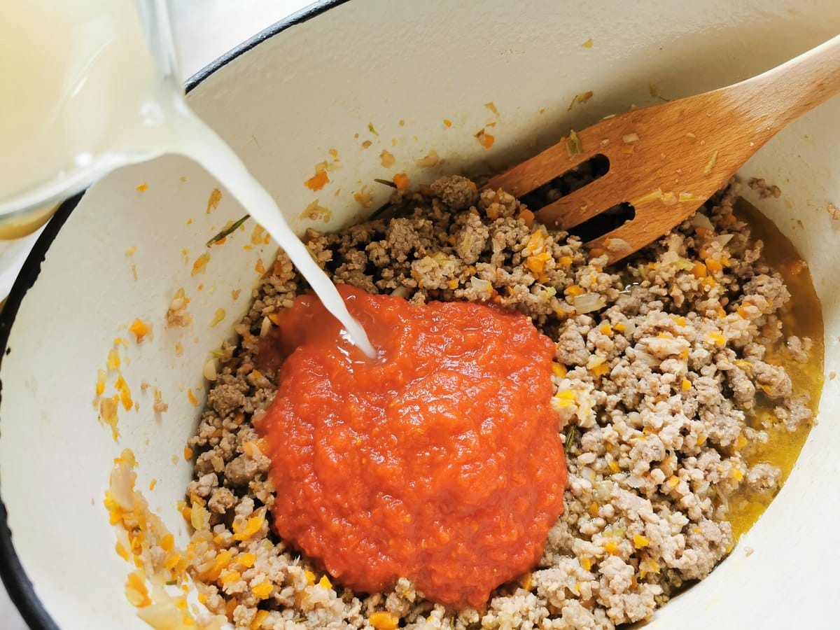 Tomato passata and vegetable broth added to beef sausage ragu in Dutch oven.