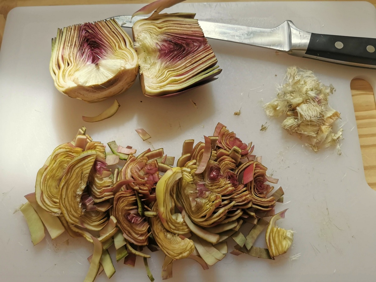 Cleaned and sliced artichokes on white chopping board.