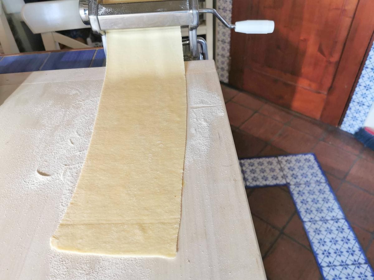 Sheet of pasta dough rolling out of pasta machine.