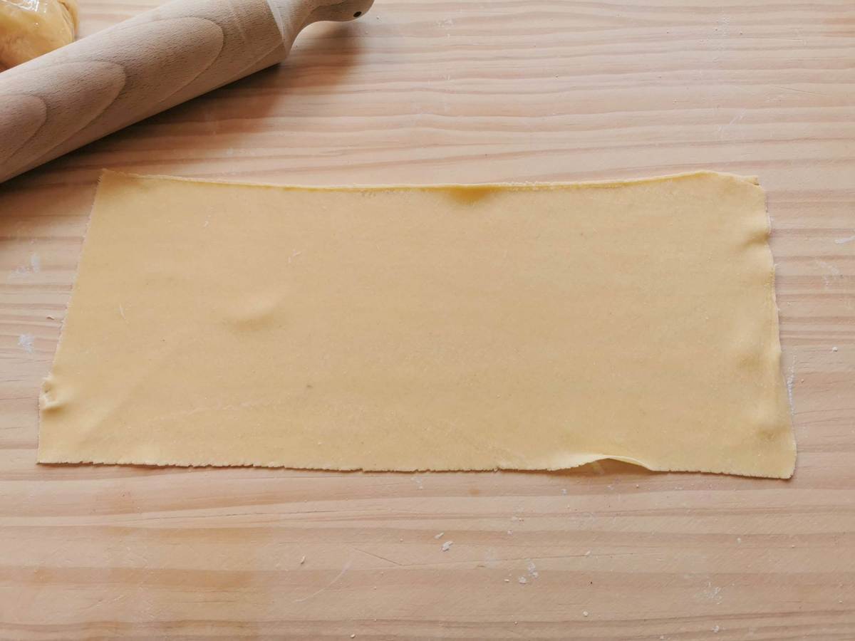 Sheet of egg pasta dough on wooden board.