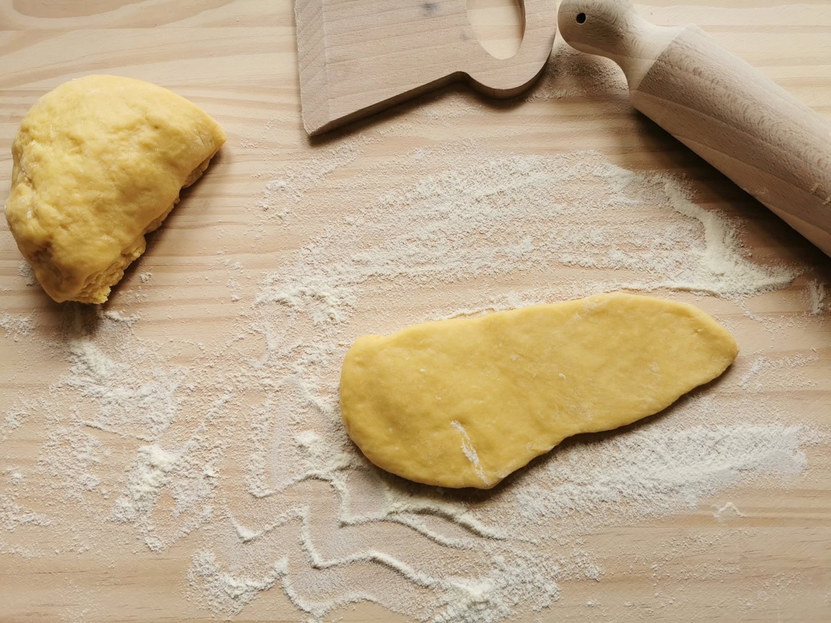 Piece of flattened tagliatelle pasta dough on flour dusted wooden board.