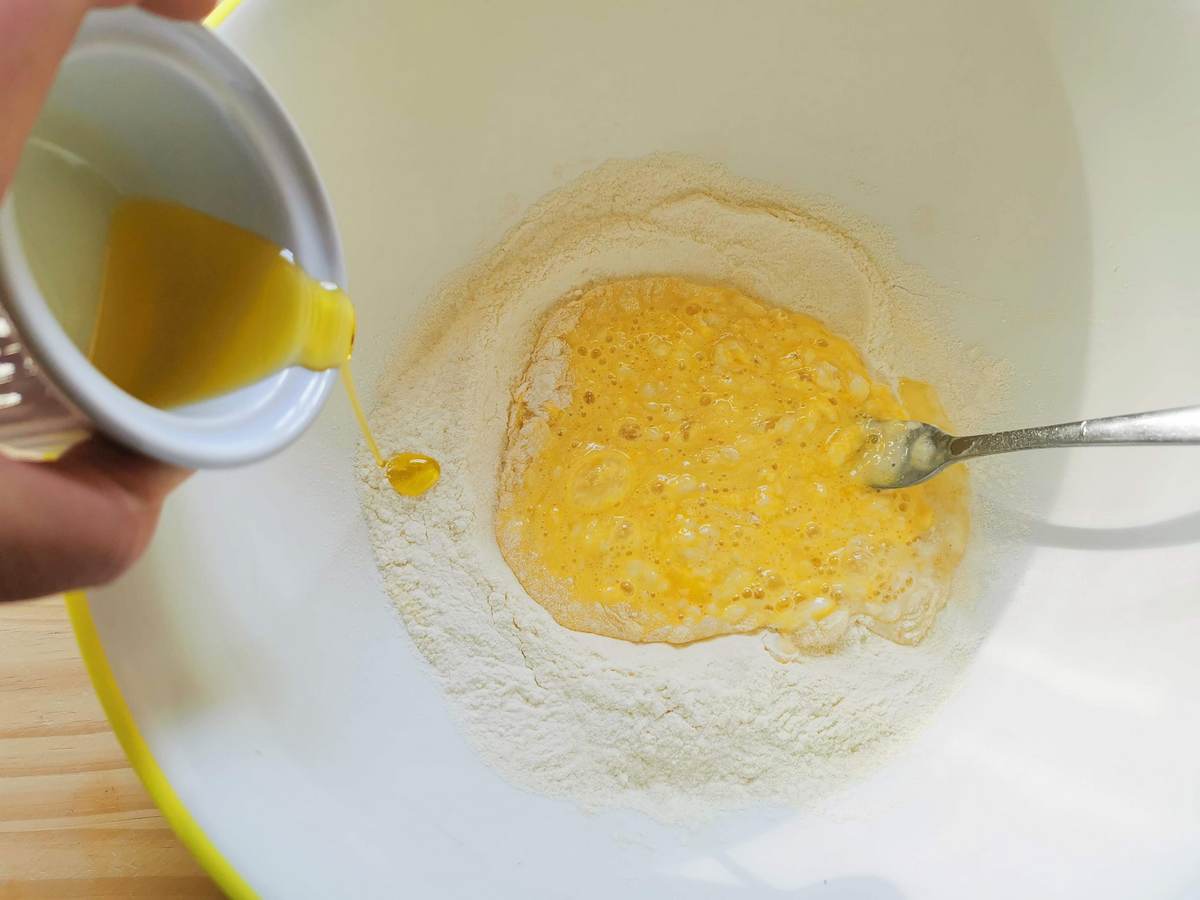 Olive oil poured into bowl with beaten eggs and flour.