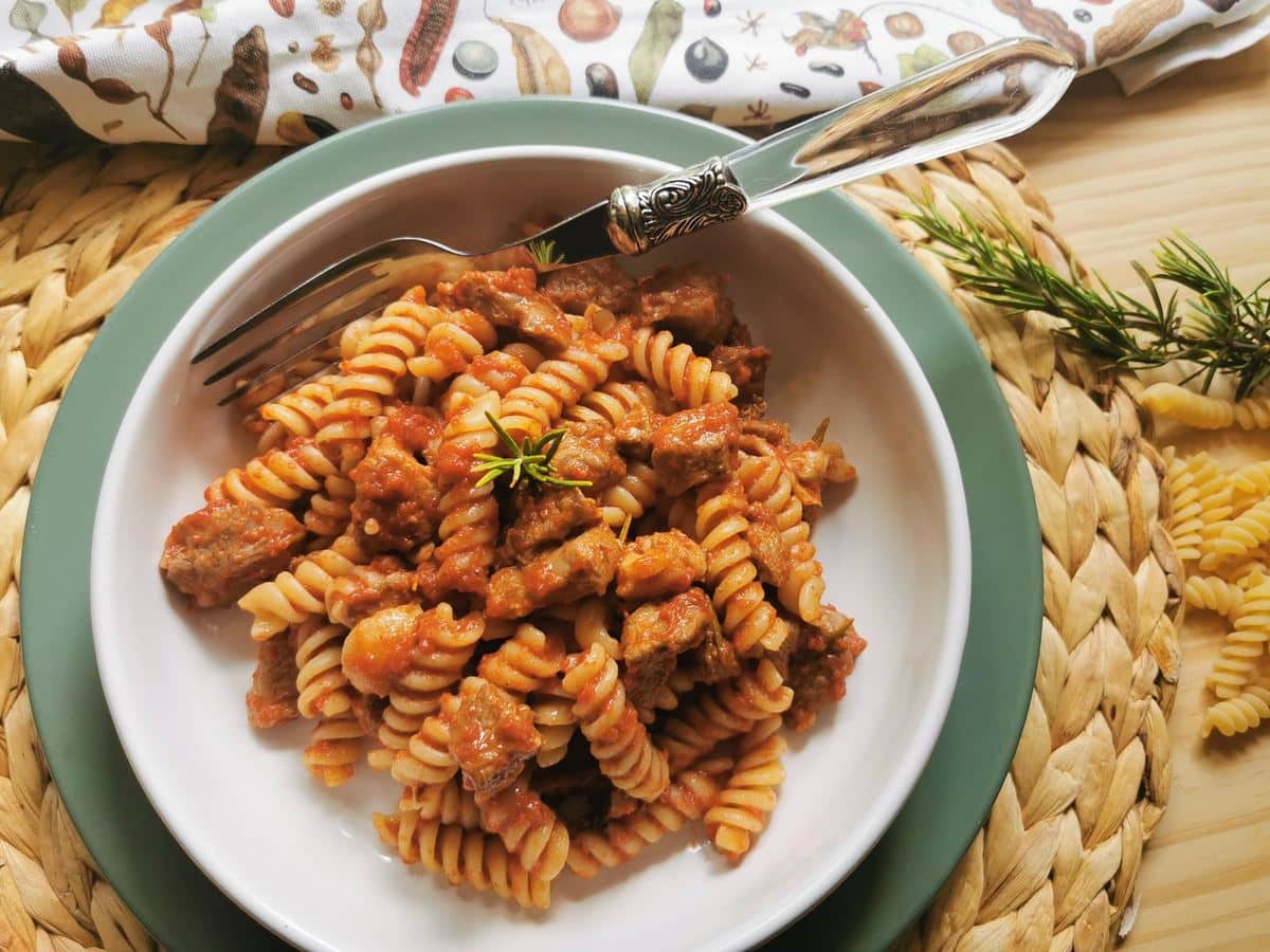 Lamb ragu and paste in a bowl with a sprig of rosemary.