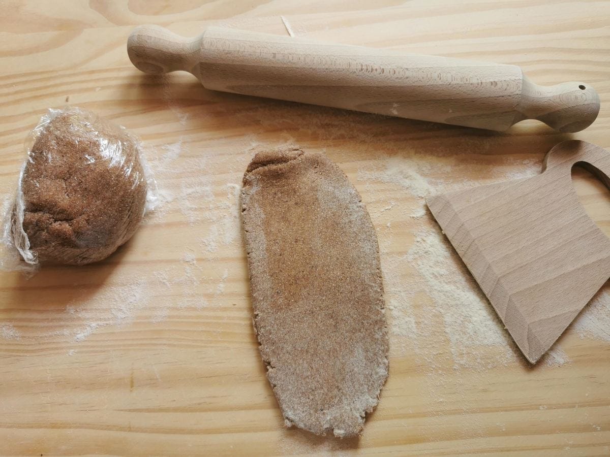 A piece of flattened chestnut pasta dough on work surface with rolling pin.