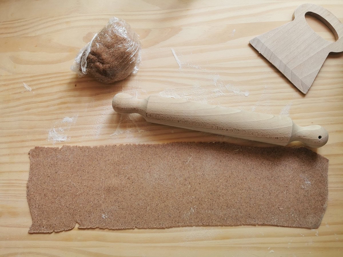 A rolled out sheet of chestnut maltagliati dough on wood work surface with rolling pin.