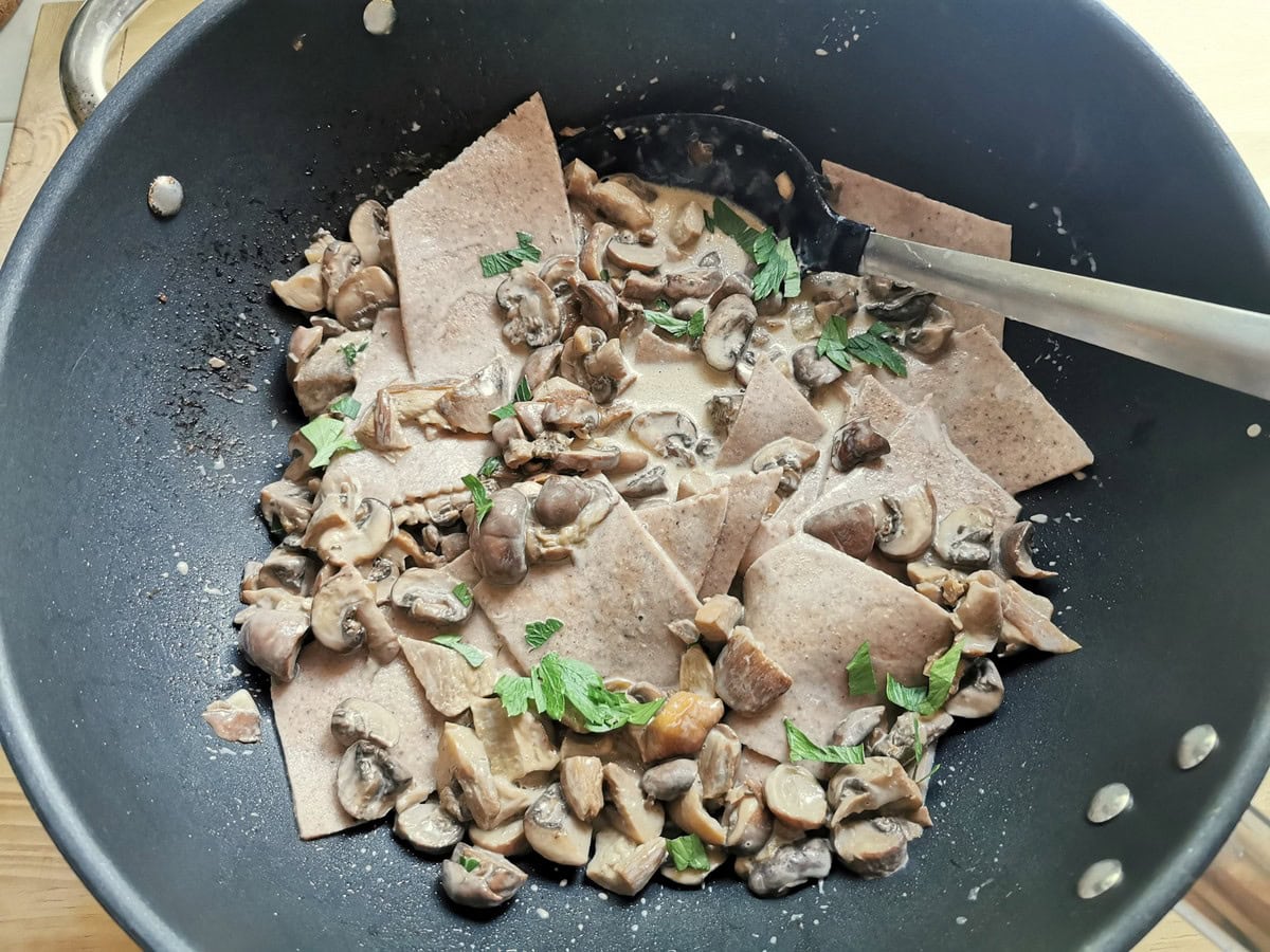 Cooked chestnut maltagliati pasta in skillet with mushroom sauce.