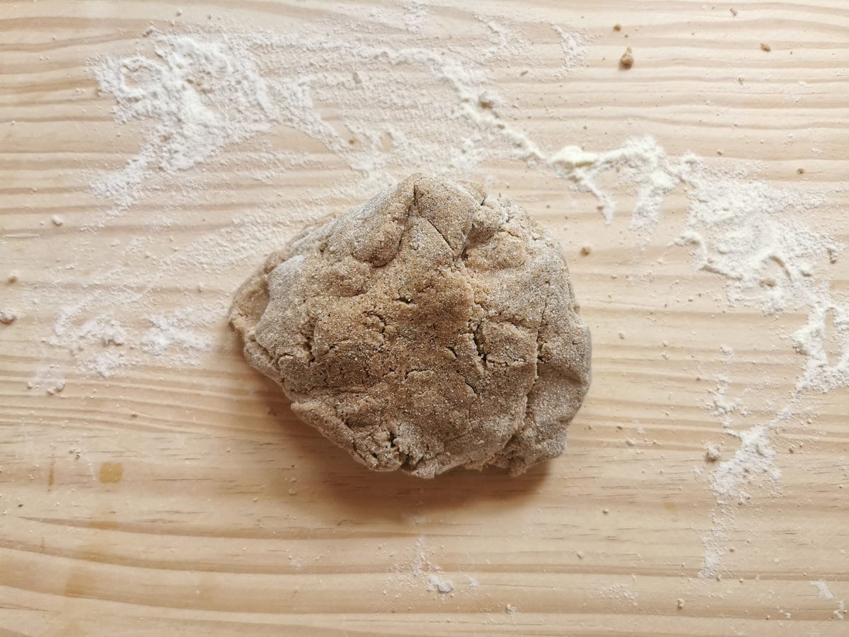 Rough ball of chestnut pasta dough on flour dusted work surface.