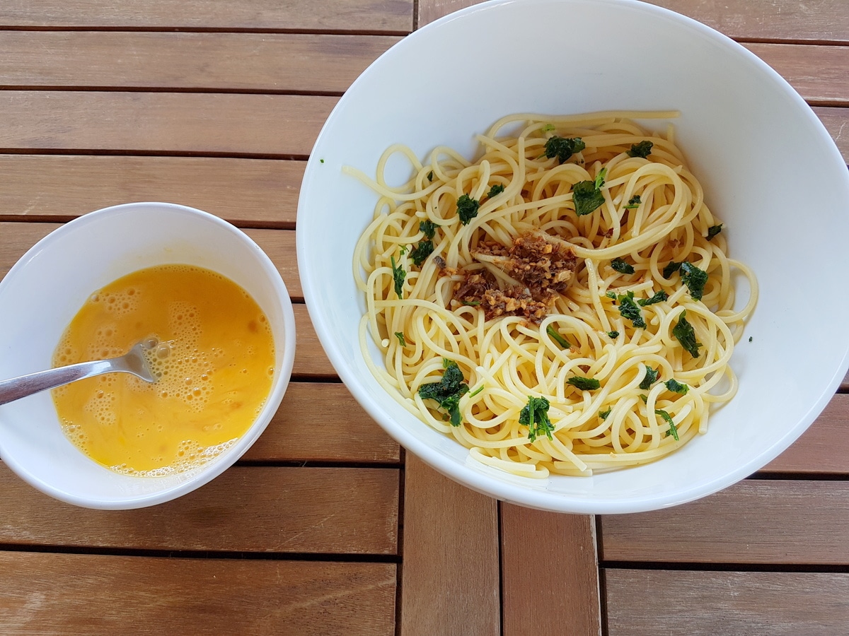 Cooked pasta, and the garlic, anchovies oil in a bowl. Another bowl with beaten eggs.