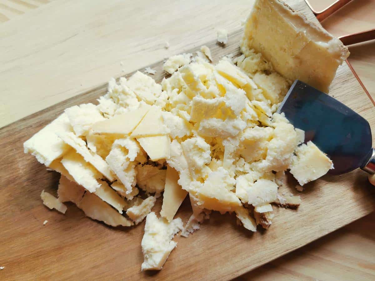 Castelmagno cheese cut into small pieces on wood cheese board.