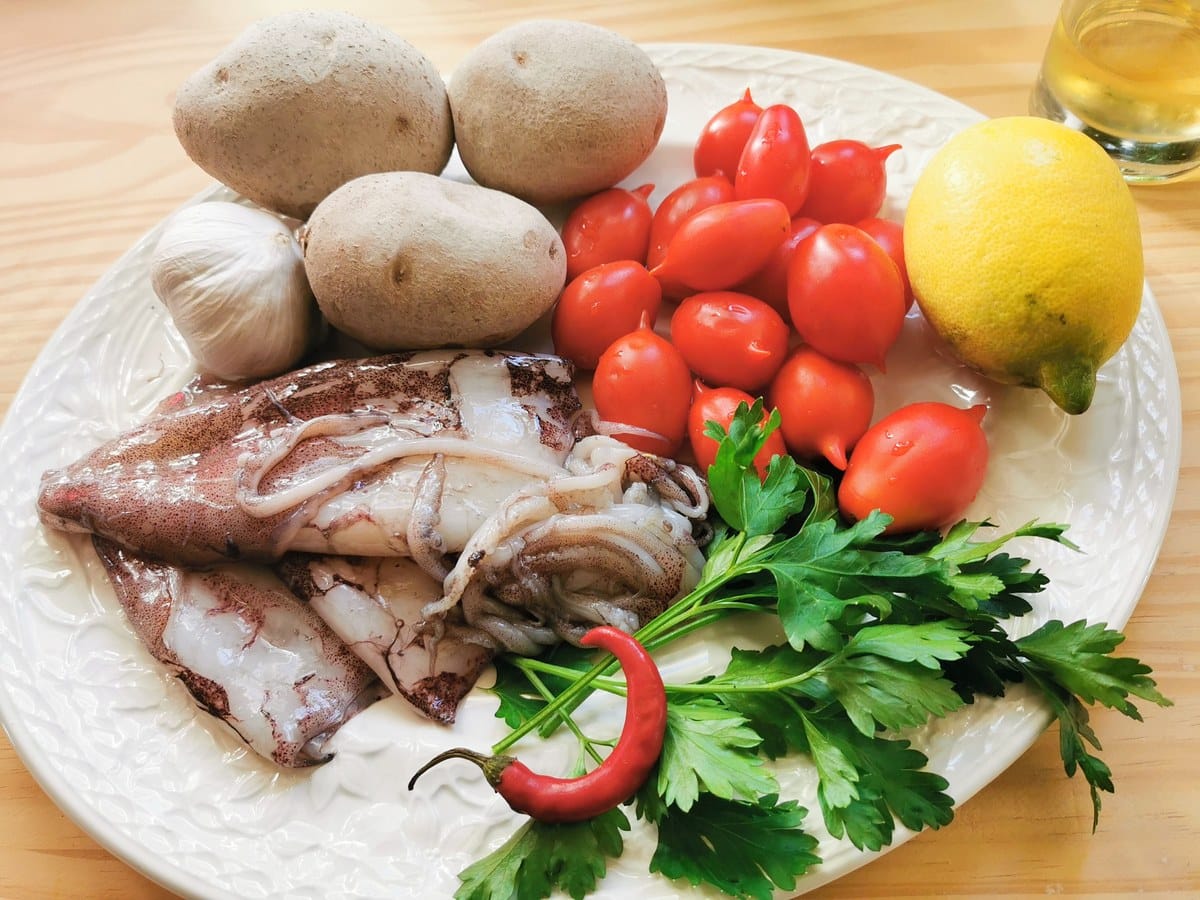 Squid, potatoes, garlic, cherry tomatoes, chili, lemon and white wine on a kitchen table.