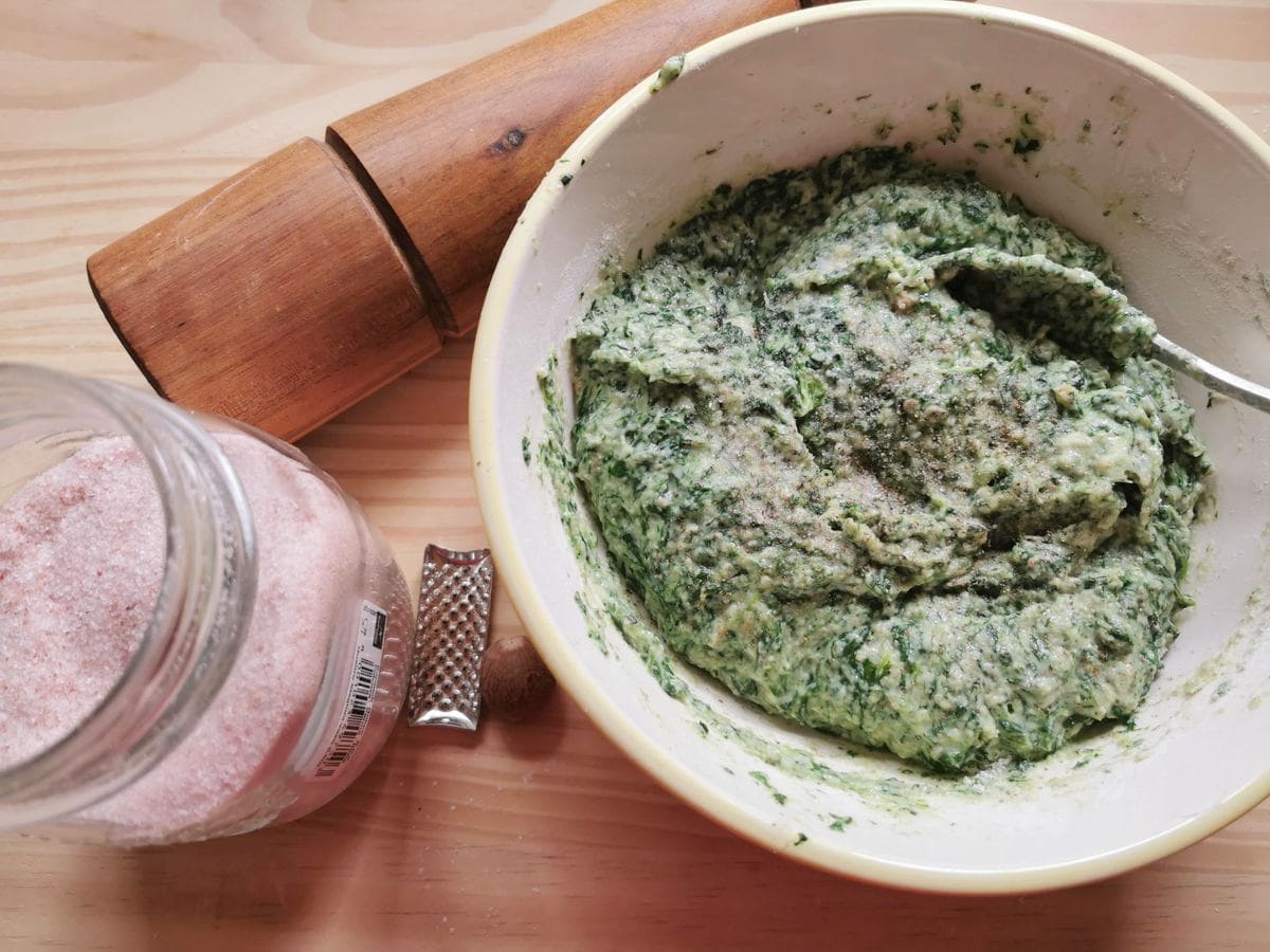 Salt, pepper and nutmeg added to ready spinach and bread gnocchi.