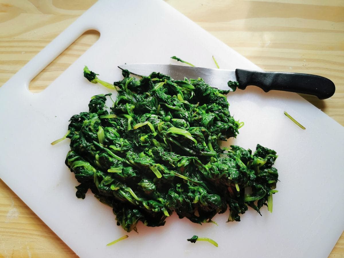 Chopped cooked erbette on white chopping board.