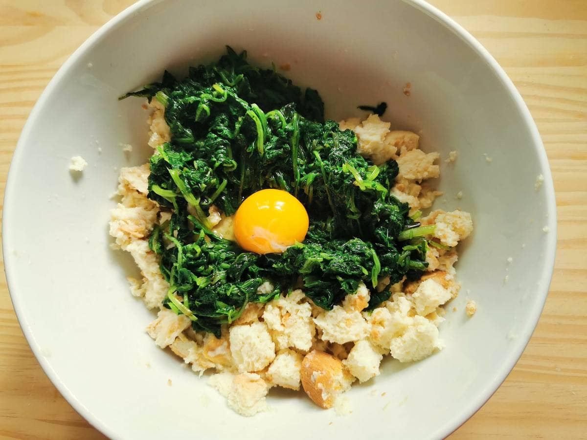 Milk soaked bread in white bowl with chopped erbette and an egg yolk.