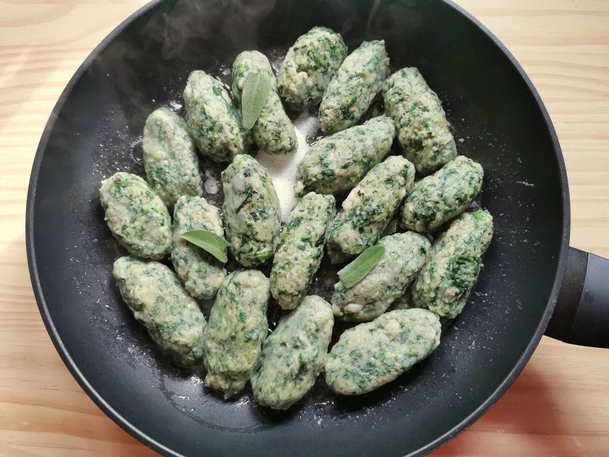 Cooked strangolapreti spinach and bread gnocchi in frying pan with butter and sage.