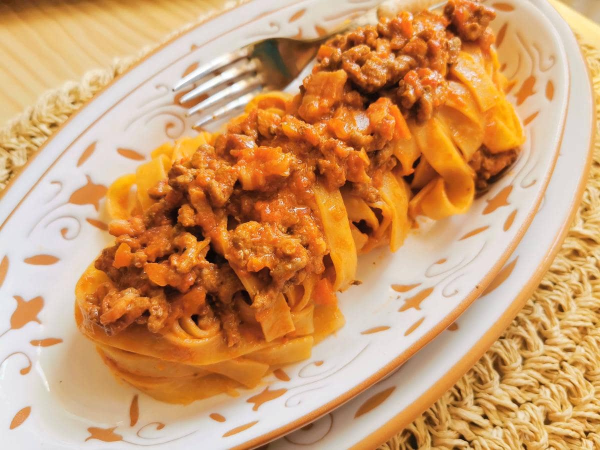 Tagliatelle with Bolognese ragu on white and terracotta plate.